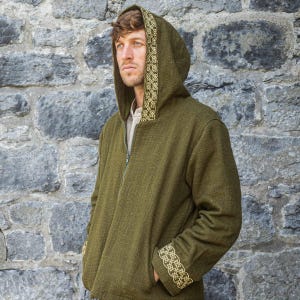 May include: An olive green hooded jacket featuring a full-length front zipper and long sleeves. The hood trim and sleeve cuffs are decorated with a light-colored, intricate woven knotwork pattern. The jacket has a textured, woven fabric construction.