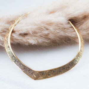 May include: A gold-toned choker necklace with a delicate floral pattern. The necklace is made of metal and has a curved shape.