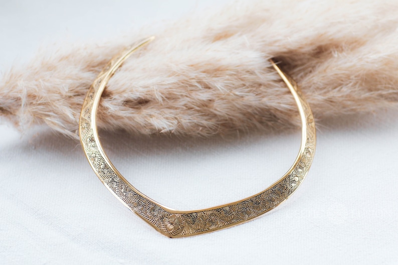 May include: A gold-toned choker necklace with a delicate floral pattern. The necklace is made of metal and has a curved shape.