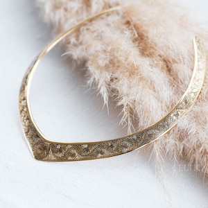 May include: A gold-toned metal necklace with an intricate floral design. The necklace is lying on a soft, fluffy surface.