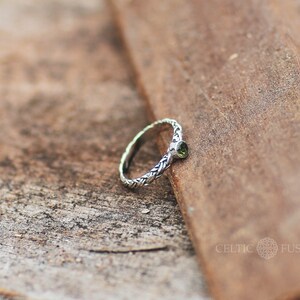 May include: A silver Celtic knot ring with a green gemstone. The ring is on a wooden surface.