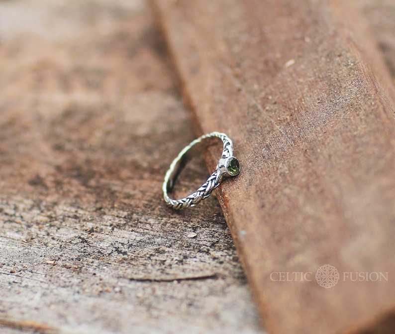 May include: A silver Celtic knot ring with a green gemstone. The ring is on a wooden surface.