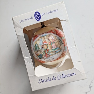 May include: Vintage Christmas bauble in a box. The bauble depicts a painted scene of two children in winter clothes, with the text "NOEL 1981". The box reads "Un monde de cadeaux" and "Article de Collection".