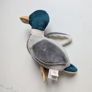 May include: A plush mallard duck toy with a dark teal head, a tan beak, a white neck ring, and a body featuring light gray and dark gray wings. A white Ty brand tag is attached to the side, displaying the name Lake and product information.