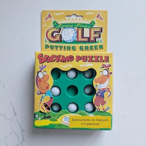 May include: A Loopy Links Golf Putting Green stacking puzzle in a yellow box. The box features cartoon characters, the text "Loopy Links GOLF PUTTING GREEN" and "STACKING PUZZLE", and a green grid containing several white dimpled golf balls.