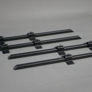 May include: Six black metal table legs with a rectangular design. Each leg has a flat base and a bracket with a screw. The legs are arranged on a gray surface.