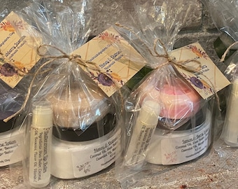 May include: Four gift bags containing various bath and body products. Each bag includes a jar of lotion, a bar of soap, and a lip balm. The labels on the jars read "Blackberry Jasmine", "Honey & Orange", "Lemon & Berry", and "Lavender & Sage".