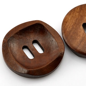 May include: Two brown wooden buttons with two slits each. The buttons are round and have a slightly raised edge.