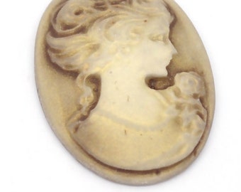 May include: A cameo featuring a woman's profile in white with a brown background. The woman is wearing a dress and has her hair pulled back.