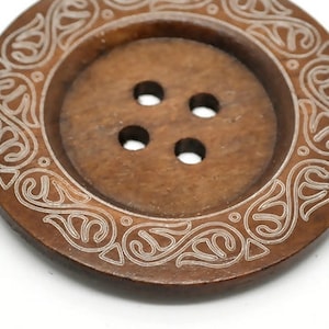 May include: A brown wooden button with a decorative white floral design around the edge. The button has four holes in the center.