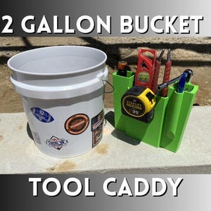 May include: A white 2-gallon bucket with stickers and a green tool caddy. The caddy holds a tape measure, level, pens, and other tools. Text on the image reads "2 GALLON BUCKET" and "TOOL CADDY".