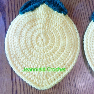 May include: Two crocheted lemon-shaped pot holders with green leaves and a loop for hanging. The pot holders are yellow and have a textured surface. The text "Jeannield Crochet" is visible on one of the pot holders.