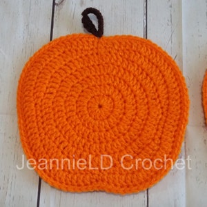 May include: Two orange crocheted pumpkins with brown stems. The pumpkins are round and have a textured surface. The pumpkins are on a white wooden background.  JeannieLD Crochet