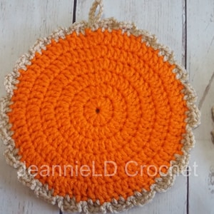 May include: Two crocheted orange and beige pot holders with a scalloped edge. The pot holders are round and have a center hole. The text "deannieLD Crochet" is visible on the bottom of one pot holder.