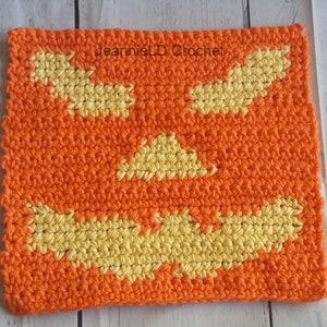 Pode incluir: Um pano de cozinha de crochê laranja e amarelo com um design de rosto de abóbora. "JeannieLD Crochet" está escrito na parte superior central do pano de cozinha.