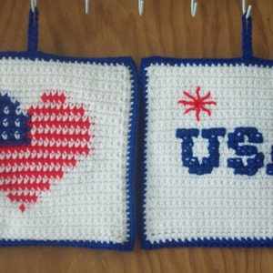 May include: Two crocheted pot holders with a patriotic theme. One pot holder features a red, white, and blue heart with stars. The other pot holder features the word "USA" in blue with red stars.