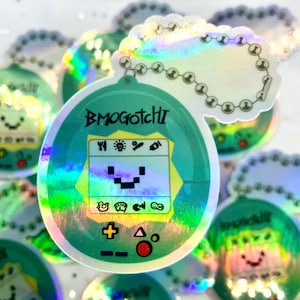 May include: A holographic green and white sticker of a Tamagotchi-like toy with the text "Bmogotchi" on it. The sticker has a chain attached to it.