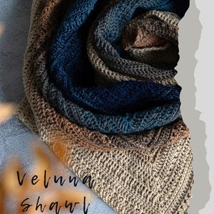 May include: A crocheted shawl in shades of beige, brown, and blue. The text "Veluna shawl" and "CROCHET PATTERN PDF" are visible. The shawl is folded, showcasing the textured stitch pattern and color gradient.