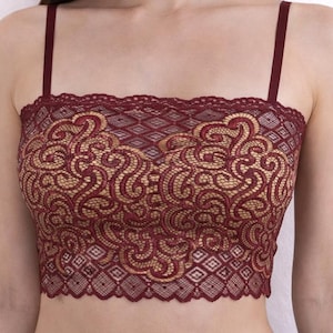 May include: A burgundy lace crop top with adjustable straps. The intricate lace design features a gold underlay, creating a contrasting pattern. The top has a scalloped edge along the neckline and bottom hem, adding a delicate touch to the garment.