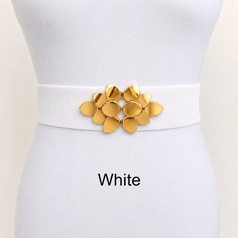 Puede incluir: Un cintur&oacute;n el&aacute;stico blanco con una hebilla central de metal dorado en forma de racimo de p&eacute;talos superpuestos. La palabra White est&aacute; impresa en texto negro debajo del cintur&oacute;n sobre el fondo liso.