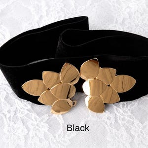 Puede incluir: Un cintur&oacute;n ancho de color negro con una hebilla grande de metal dorado en forma de dos grupos de hojas superpuestas. El cintur&oacute;n est&aacute; hecho de una tela oscura y suave, y la palabra Black est&aacute; impresa en letras negras peque&ntilde;as al centro.