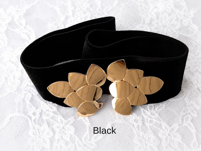 Puede incluir: Un cintur&oacute;n ancho de color negro con una hebilla grande de metal dorado en forma de dos grupos de hojas superpuestas. El cintur&oacute;n est&aacute; hecho de una tela oscura y suave, y la palabra Black est&aacute; impresa en letras negras peque&ntilde;as al centro.