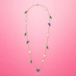 May include: A gold-colored necklace featuring a delicate design of butterflies, flowers, and leaves. The butterflies have blue and white enamel details, while the leaves are green. The necklace is displayed against a pink background.