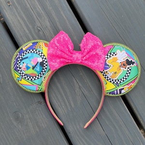 May include: A headband featuring two circular ears with a vibrant 1990s-inspired graphic print of Goofy and Max. The ears are bordered with green glitter piping. A large, bright pink sequined bow is centered between the ears on the headband.