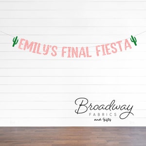May include: A pink glitter banner that reads "EMILY'S FINAL FIESTA" with green cactus accents. The banner is strung across a white wall with a wooden floor. The Broadway Fabrics and Gifts logo is at the bottom.