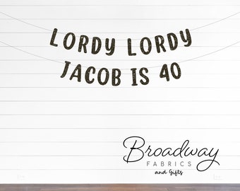 May include: A decorative banner featuring dark, glittery, textured letters strung on thin lines. The text reads LORDY LORDY JACOB IS 40, arranged in two horizontal rows. The letters have a distinct, slightly rounded, bold typeface with a sparkling finish.
