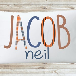 May include: White pillow with the name "JACOB neil" written in colorful, patterned letters. The letters are in a playful, handwritten style.