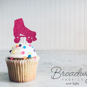 Peut inclure: Décor de cupcake en forme de patin à roulettes rose pailleté. Le décor est sur un cupcake blanc avec des pépites colorées.