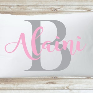 May include: A white pillow with a grey letter "B" and the name "Alaini" written in pink cursive.