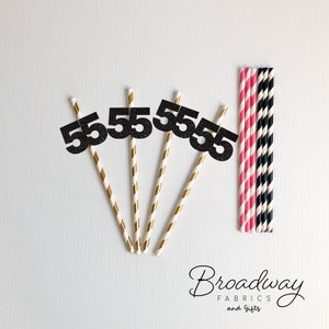 May include: Five black glitter straws with the number "55" on each straw. The straws are gold and white striped. There are also pink and black striped straws in the background.