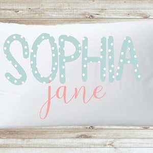 May include: White pillowcase with the name "Sophia Jane" printed on it. The name "Sophia" is in light blue with white polka dots and the name "Jane" is in pink cursive.