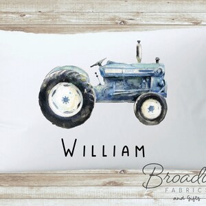 K&ouml;nnte beinhalten: Ein wei&szlig;er Kissenbezug mit einer Aquarell-Illustration eines Vintage-Traktors in Blau- und Gr&uuml;nt&ouml;nen. Der Traktor tr&auml;gt den Schriftzug "FORD" an der Seite. Der Name "WILLIAM" ist unter dem Traktor gedruckt.