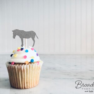May include: A gray glitter donkey cupcake topper on a white cupcake with colorful sprinkles.