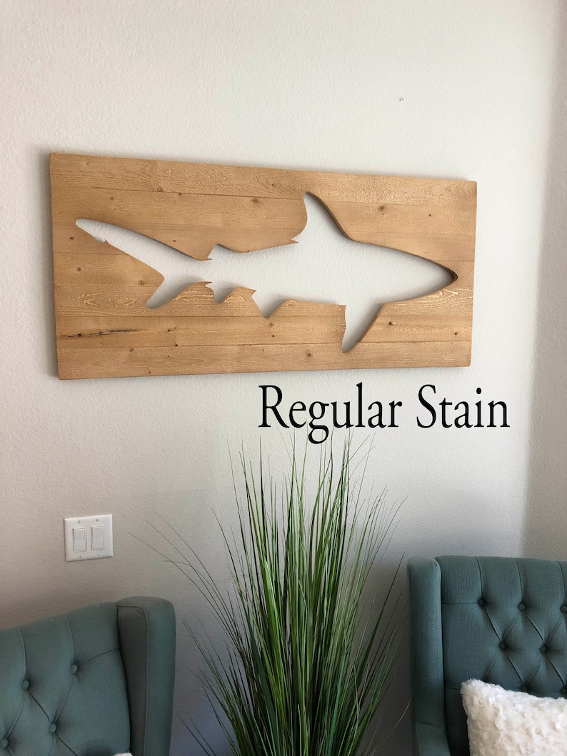 May include: A wooden wall art piece featuring a cutout of a shark silhouette. The wood is stained a light brown colour. The text "Regular Stain" is printed below the art piece.