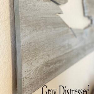 May include: Close-up of a grey distressed wood sign with a cutout shape. The sign has a rustic, weathered look.