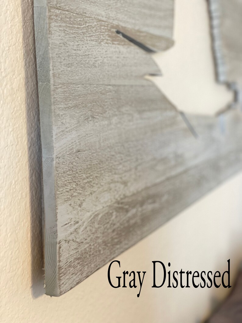 May include: Close-up of a grey distressed wood sign with a cutout shape. The sign has a rustic, weathered look.
