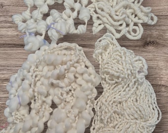 May include: Four skeins of white yarn, each with a different texture. The yarn is arranged in a pile on a wooden surface.