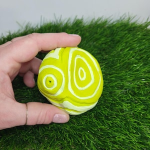 Pode incluir: Uma esfera de cerâmica amarela e branca com um padrão em espiral. A esfera tem um pequeno furo no centro.