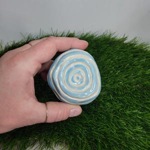 Pode incluir: Um pequeno adorno redondo de cerâmica com um padrão de espiral azul e branco. O padrão de espiral lembra uma concha.