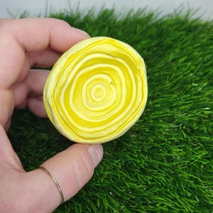 Pode incluir: Um objeto redondo e plano com um design de espiral amarelo e branco. O objeto é feito de um material suave e liso.