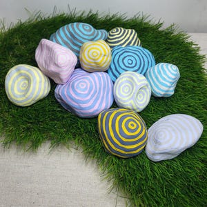 Pode incluir: Uma coleção de 10 pedras decorativas pintadas à mão com um padrão em espiral em tons de azul, amarelo, rosa e branco.