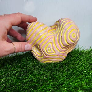 Pode incluir: Uma escultura de cerâmica rosa e amarela com um design abstrato em espiral. A escultura é texturizada e tem uma sensação áspera e orgânica.