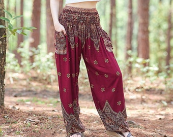 May include: A woman wearing a white t-shirt and maroon printed pants stands in a forest. The pants have a wide leg and a drawstring waist.
