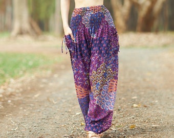 May include: A woman wearing a black crop top and colorful patterned pants walks on a dirt path in a forest.