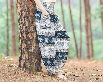 May include: A woman wearing a white crop top and patterned trousers stands in a forest. She is leaning against a tree and smiling at the camera.