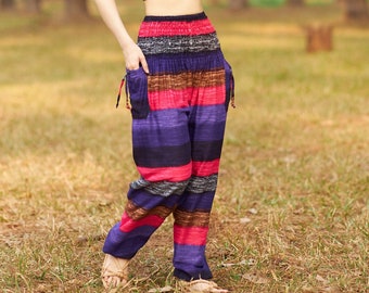 May include: A woman wearing a black sports bra and colorful striped pants stands in a forest setting. The pants have a wide leg and a drawstring waist.